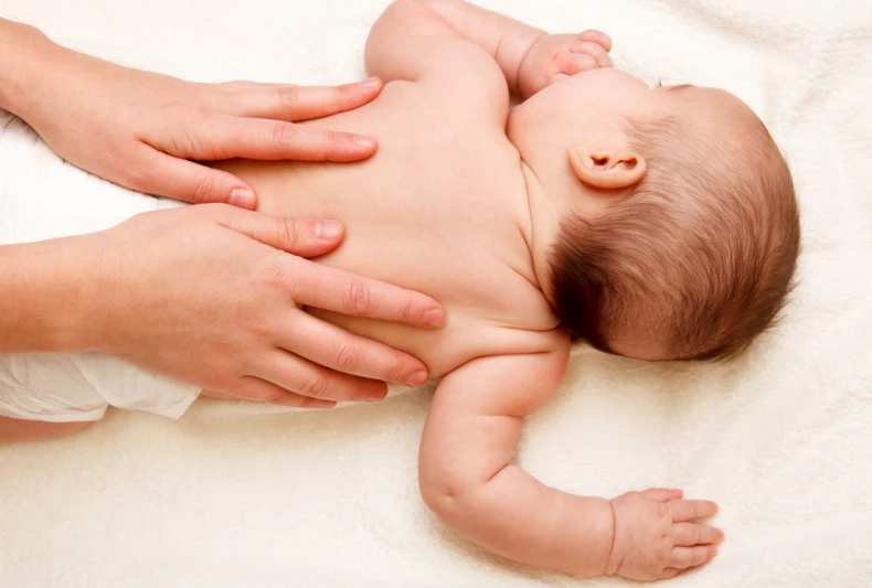 bébé en couche allongé sur le dos, 2 mains massent son dos moment de détente